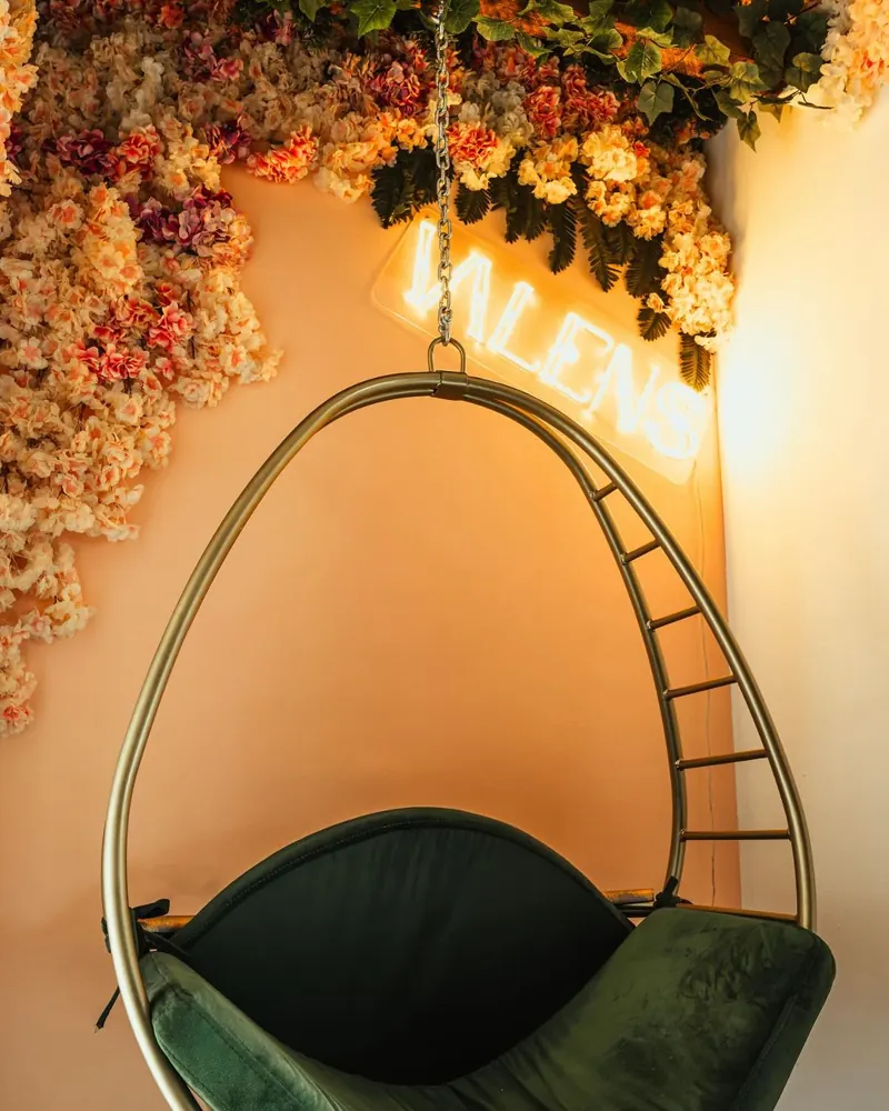 Hängesessel unter Blumendecke mit Valens Neon-Schriftzug